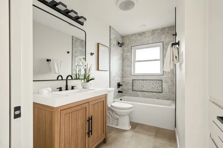Remodeled bathroom with wood vanity and tiled tub surround
